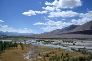 Beautiful mountain valley landscape with a winding river, trees, and a clear blue sky.
